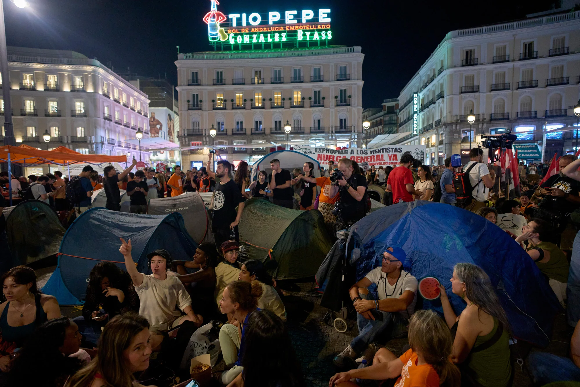 Acampada por la vivienda en la Puerta del Sol de Madrid, con manifestantes, tiendas de campaña y el luminoso de Tío Pepe.